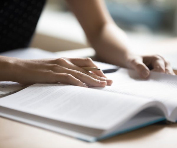 Student preparing for college test, exam, reading book, studying textbook, writing notes, making summary for class report. Learning workplace table, hands with pencil close up